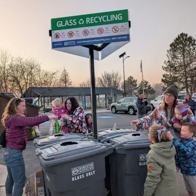 A group of people standing around trash cans recycling glass