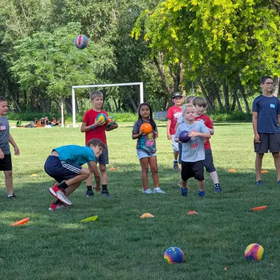 Youth playing dodgeball on grass in a park