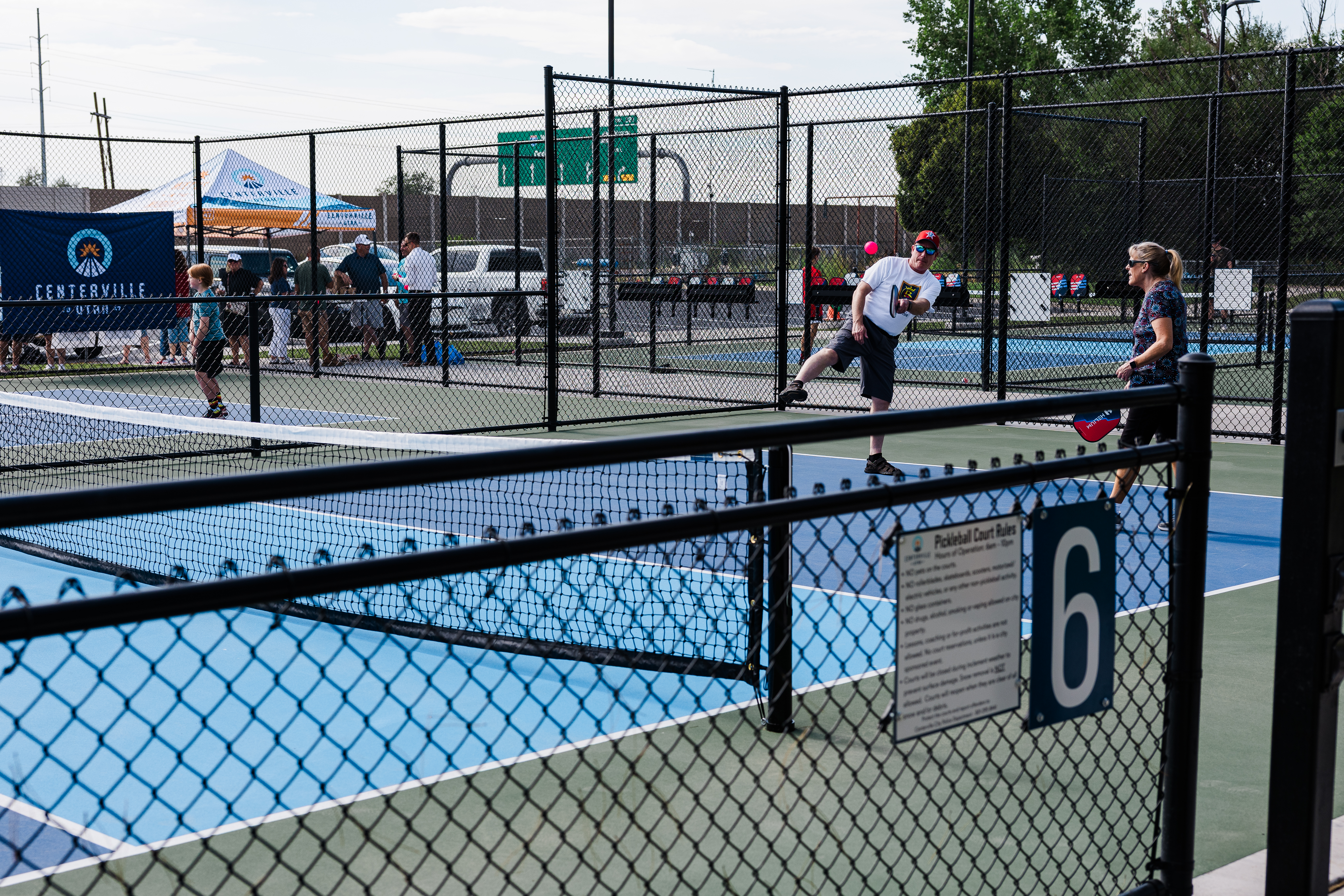 Couple playing pickleball at the court opening in Centerville surround by other full courts and a small crowd under the centerville tent.