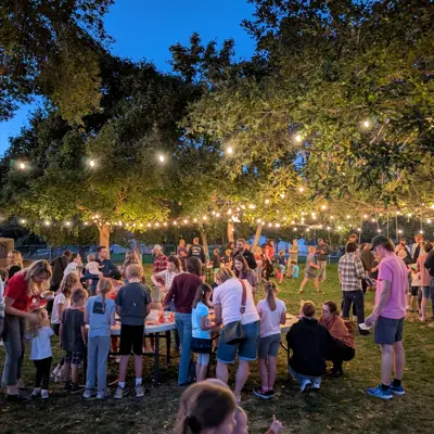 Lights strung between trees light the twlight sky while a crow of people particpate in varios fall crafts