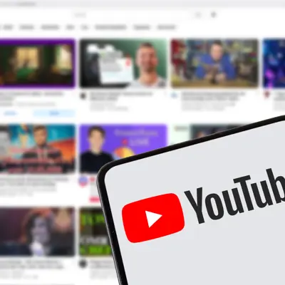 A person holding a phone with the YouTube logo on it and a YouTube Page in the background