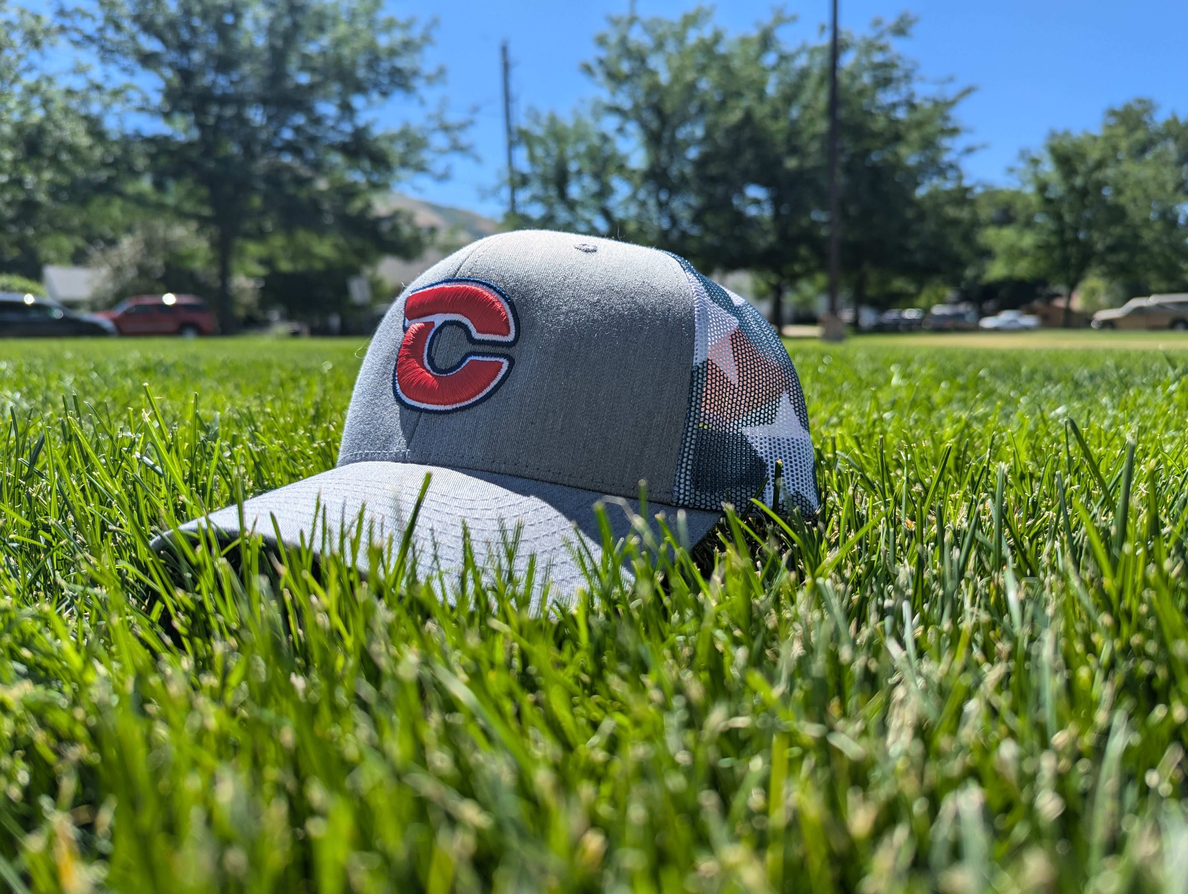 Centerville Baseball hat with rd and blue C logo under summer sunlight laying amoungst the tall green grass blades