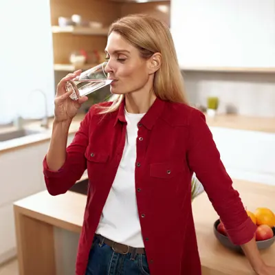 A woman drinking a glass of water from her kitchen sink