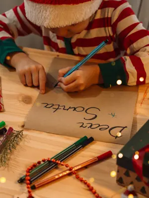Child writing a letter to santa surrounded by christmas decor