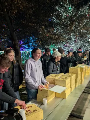 Youth chatting under a park pavilion while handing out donuts with christmas lights lighting the trees in the background