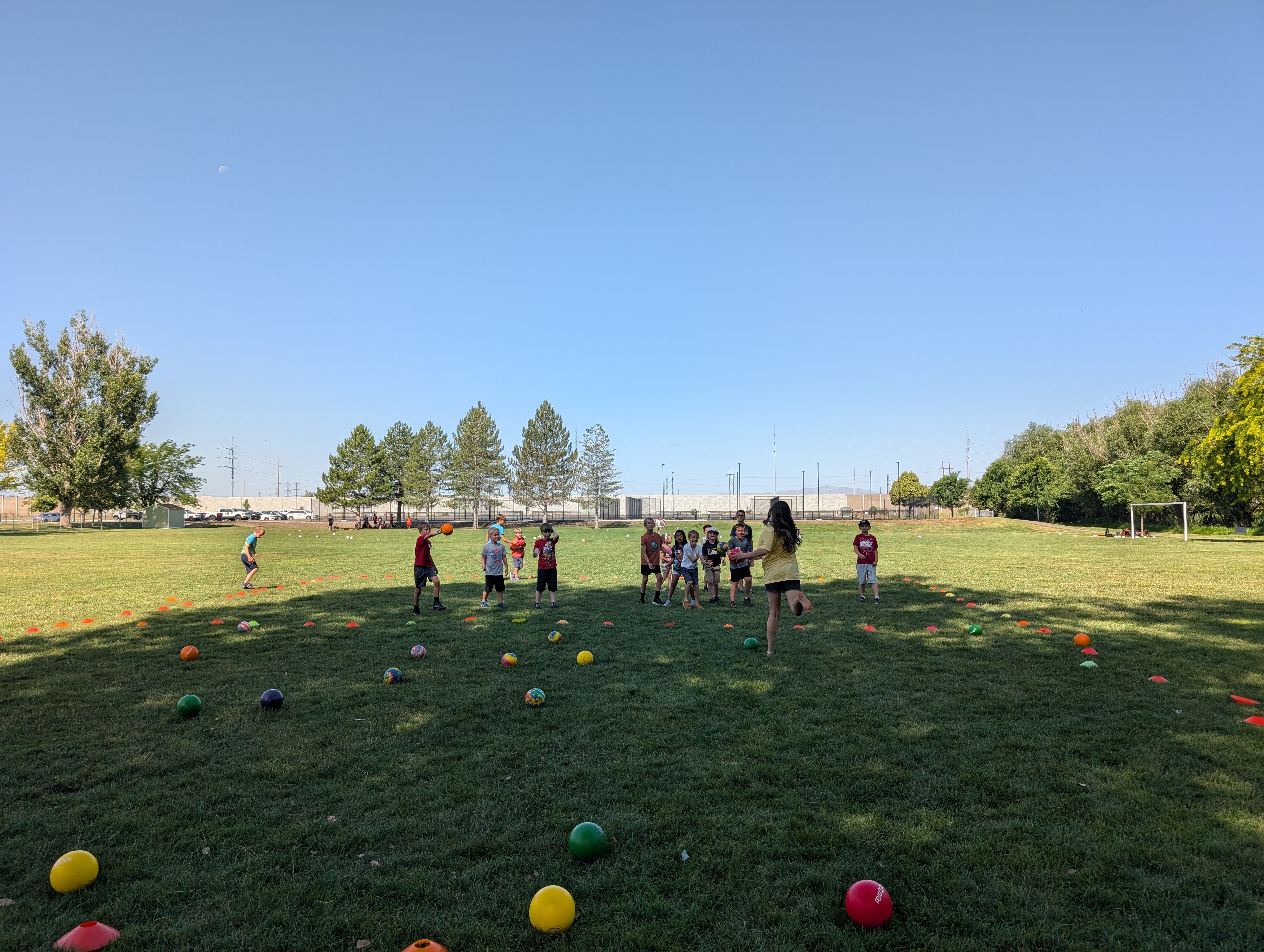 Small group of children playing dodgeball in the park on a summer morning in the shade as the sun lights the expansive park behind them
