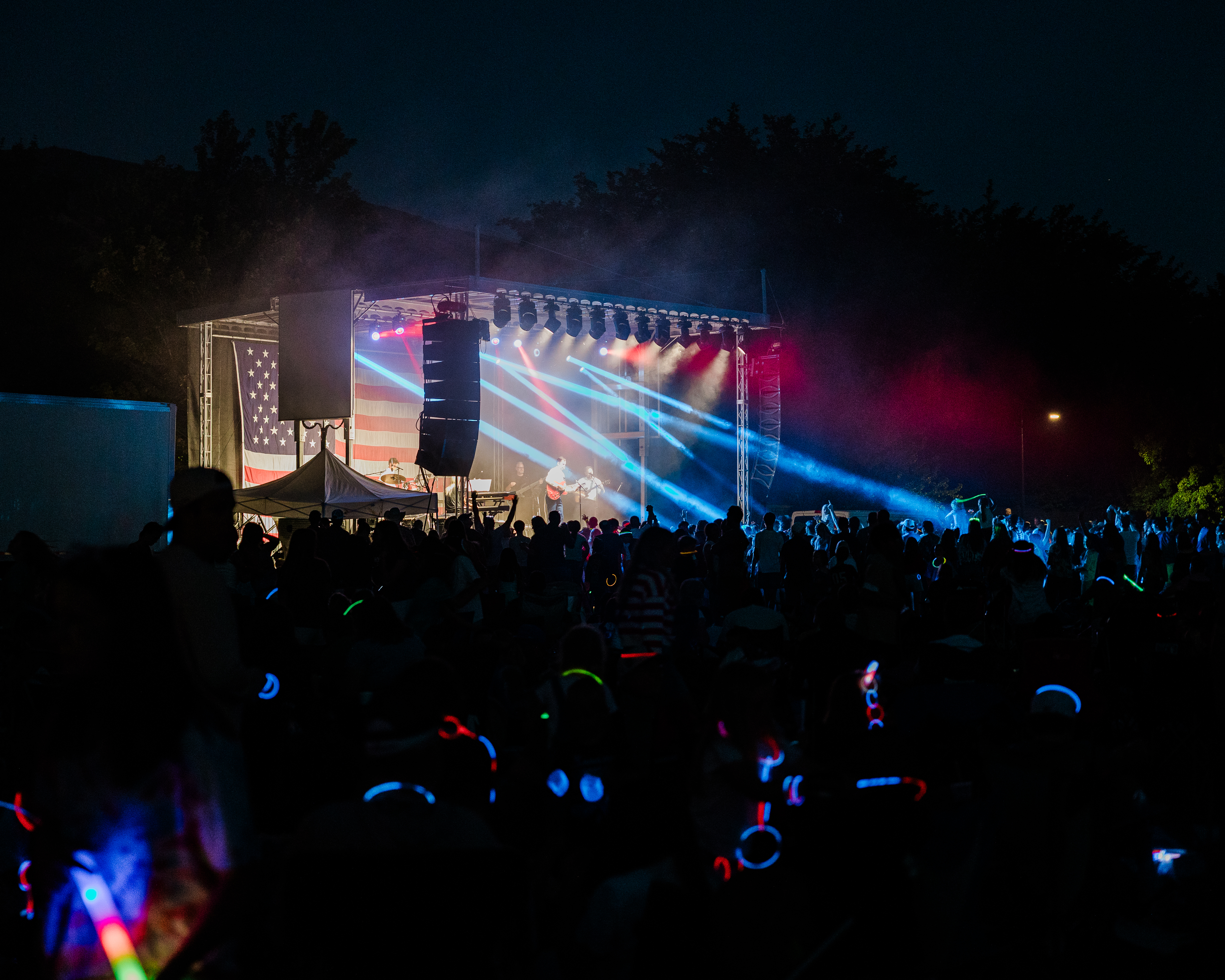 Freedom Festival Concert with stage lighting beaming out onto the active crowd with the giant american flag in the background while band plays