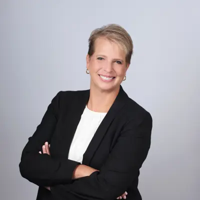 A picture of Gina Hirst in a black suit, white blouse, and smiling