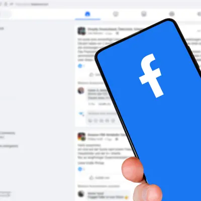 An image with a phone displaying Facebook with a Facebook page as the background