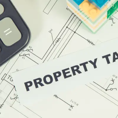 a calculator sitting on top of house plans next to some Legos with the word's property tax on top of the plans