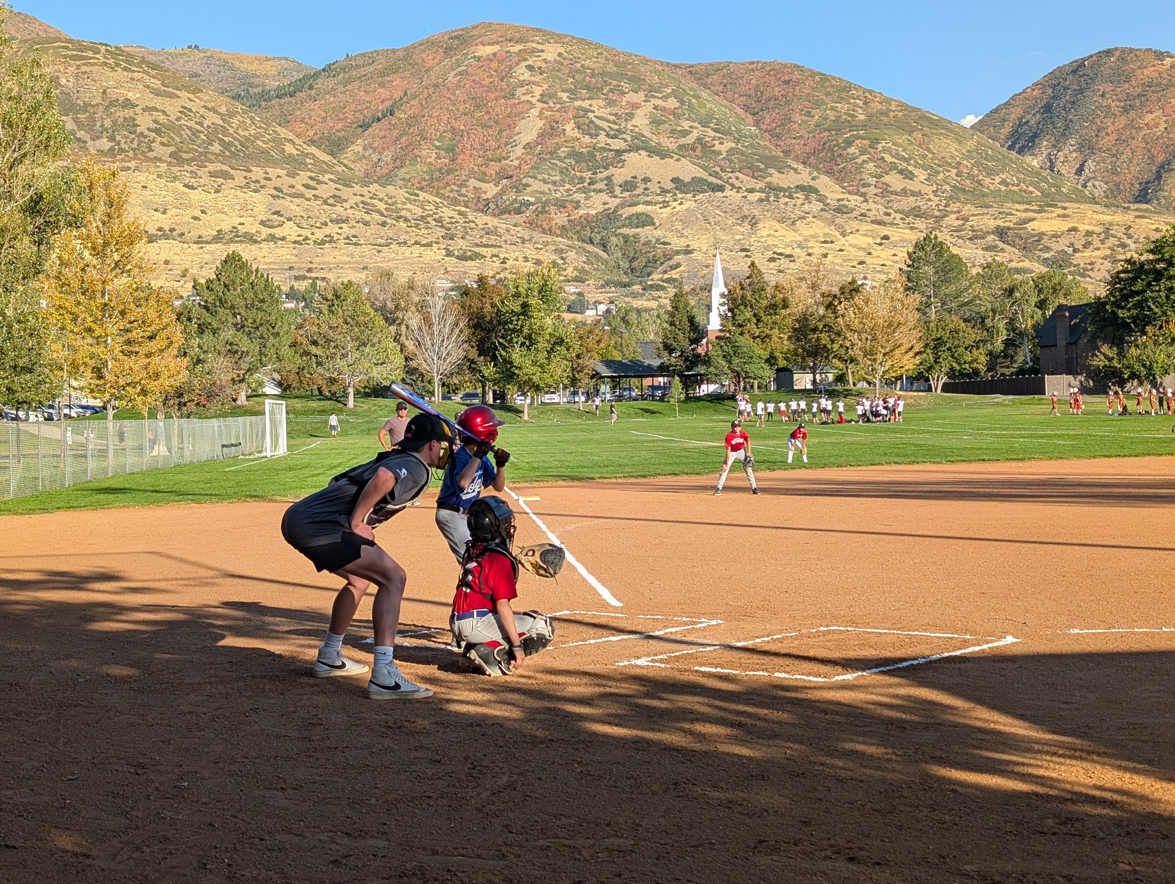 Youth baseball player at bat with pitcher and umpire waiting the pitch on a groomed baseball diamond with fall foliage in the background